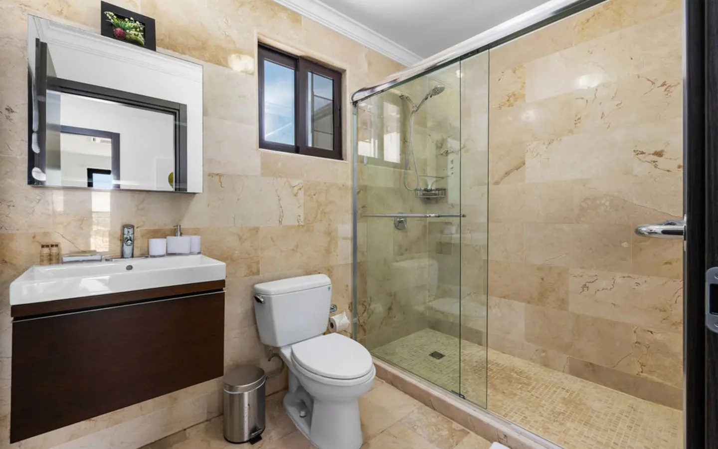 Second full bathroom finished in marble with a glass shower enclosure